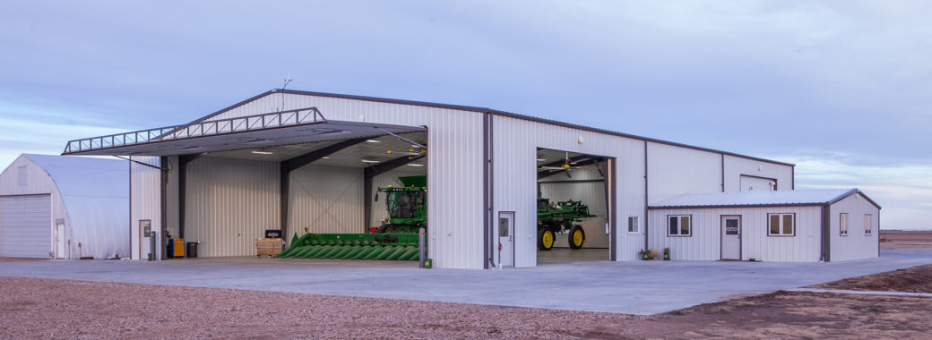 Large outdoor building with two large openings on two sides of the building housing large pieces of farm equipment