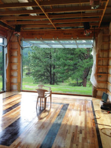 Interior view of hardwood floored building, hydraulic door open showing outside, pine trees, bright green grass