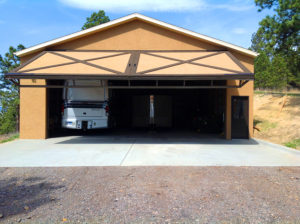 Tan and brown garage, hydraulic door half-way open, smaller camper parked inside, gravel drive