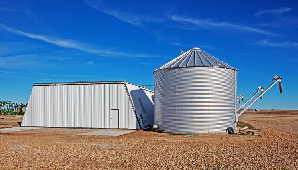 Large trapezoid-shaped meta building beside a tall grain silo in front of a deep blue sky