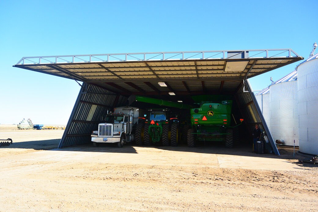 Large outdoor building with front bay door raised to show an 18-wheeler and two agricultural machines inside of the building
